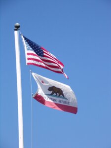 United States and California flags fly in front of a blue sky.